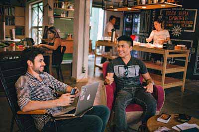 A photo of two men from different races sitting down while chatting in a cafe